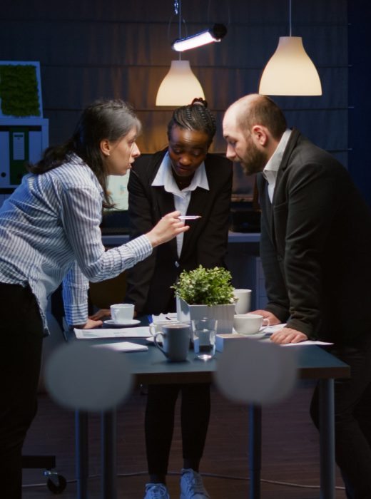 Focused leader woman enter in office meeting room lean on conference table brainstorming business company presentation late at night. Diverse multi ethnic teamwork solving management strategy